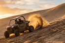 UTV rear paddle tire throwing an arc of sand while climbing a dune at golden hour