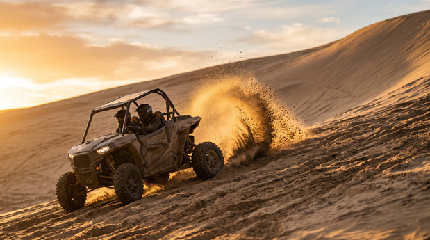 UTV rear paddle tire throwing an arc of sand while climbing a dune at golden hour