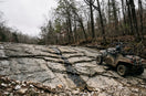 Side-by-side UTV crossing a fractured limestone shelf on a rocky Ozark hardwood forest trail