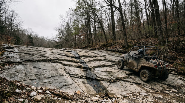 Side-by-side UTV crossing a fractured limestone shelf on a rocky Ozark hardwood forest trail