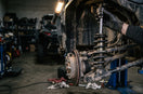 Gloved hand on a UTV coilover shock on a lift, oil and dust streaked down the body onto the spring
