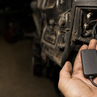 Small black GPS tracking module held in a hand in front of an open UTV dash wiring bay